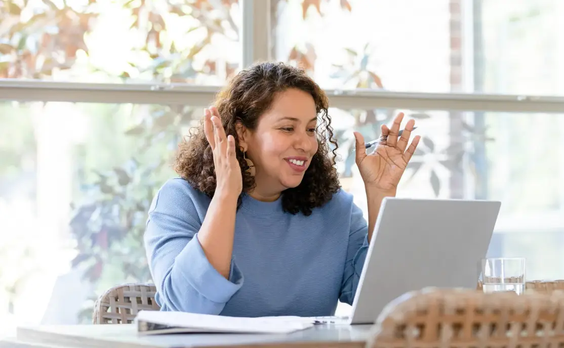 Happy latinx woman talking to someone on a laptop in front of a window