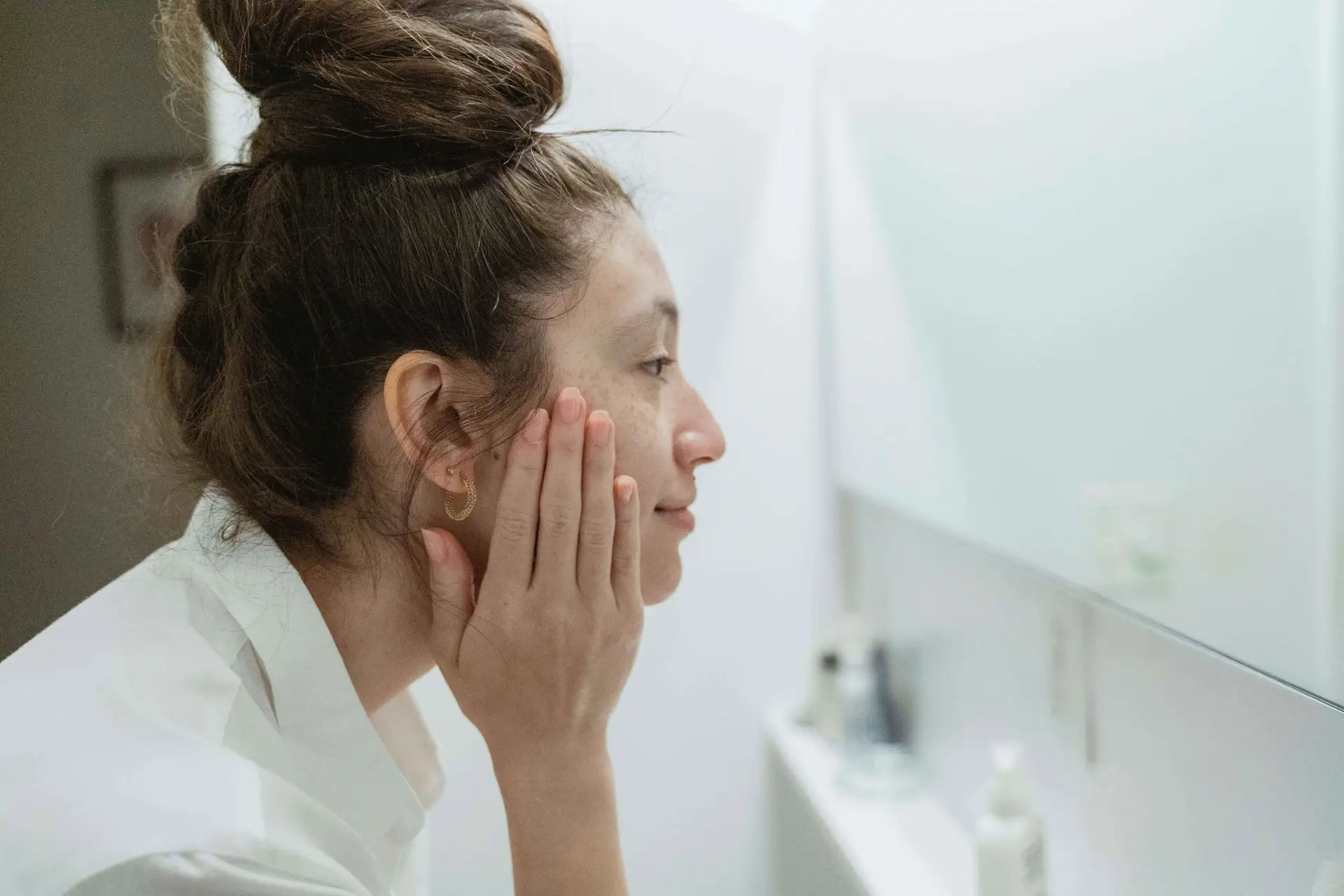 Profile of mixed race woman pressing hands to face and looking into mirror