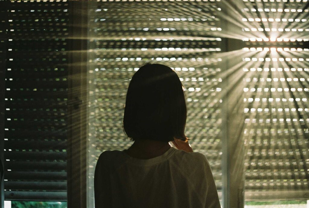 Silhouetted woman looking out a window, symbolizing a mother contemplating therapy and coaching rates for moms during postpartum.