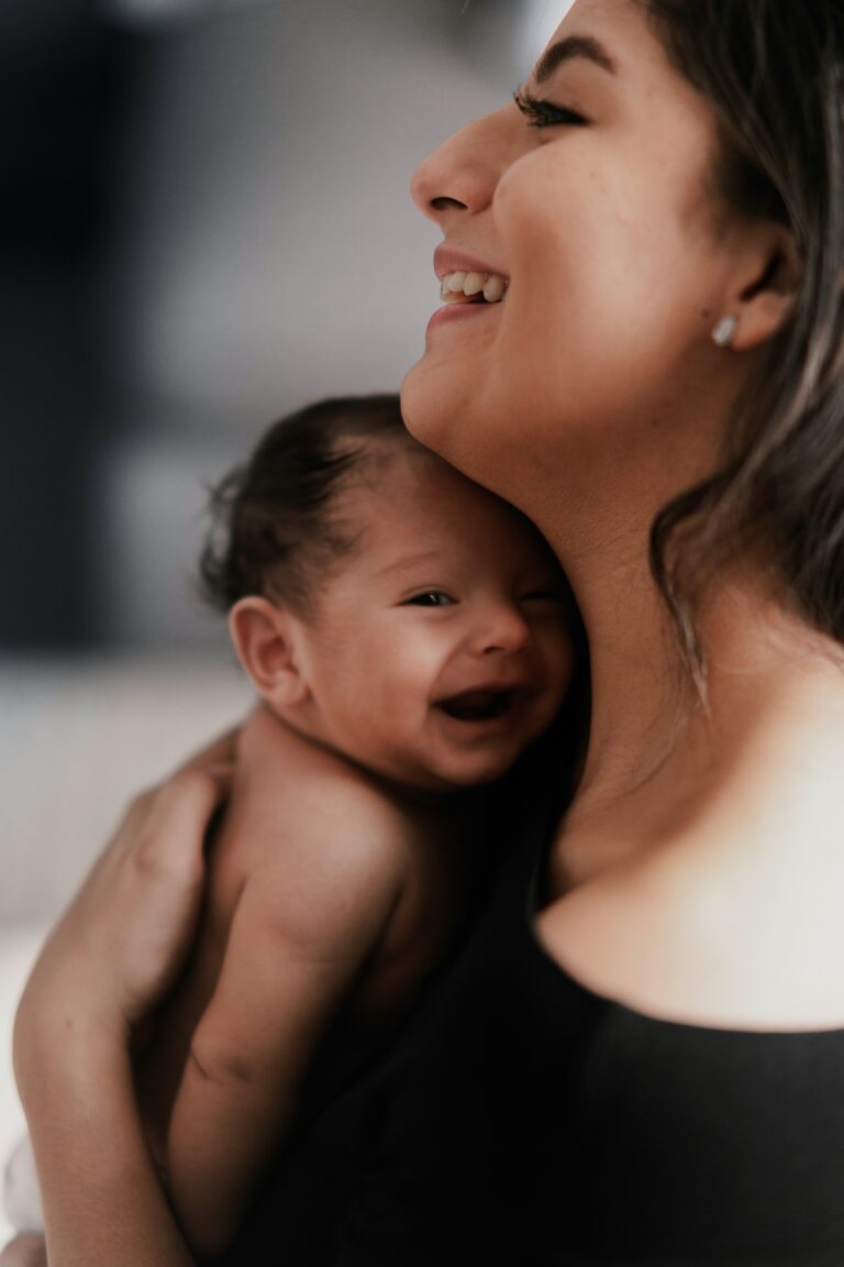 Smiling mother holding her laughing baby close, sharing a warm, joyful moment.